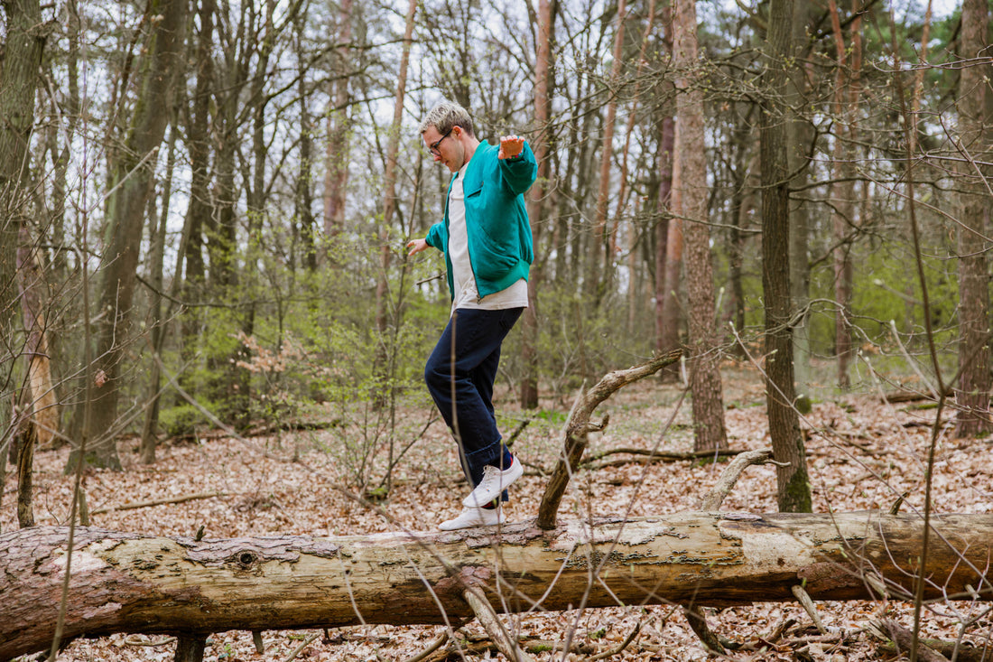 Eine Person balanciert in Wildling Minimalschuhen auf einem horizonal liegenden Baumstamm. Im Hintergrund lichter Wald.